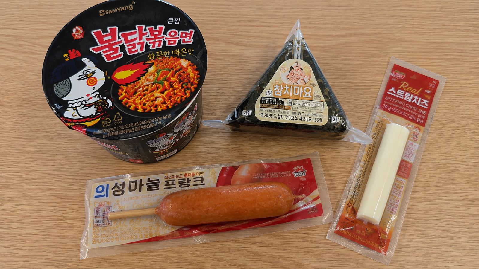 불닭볶음면, 참치마요 삼각김밥, 소시지, 스트링치즈를 나무 테이블 위에 나란히 놓은 사진
