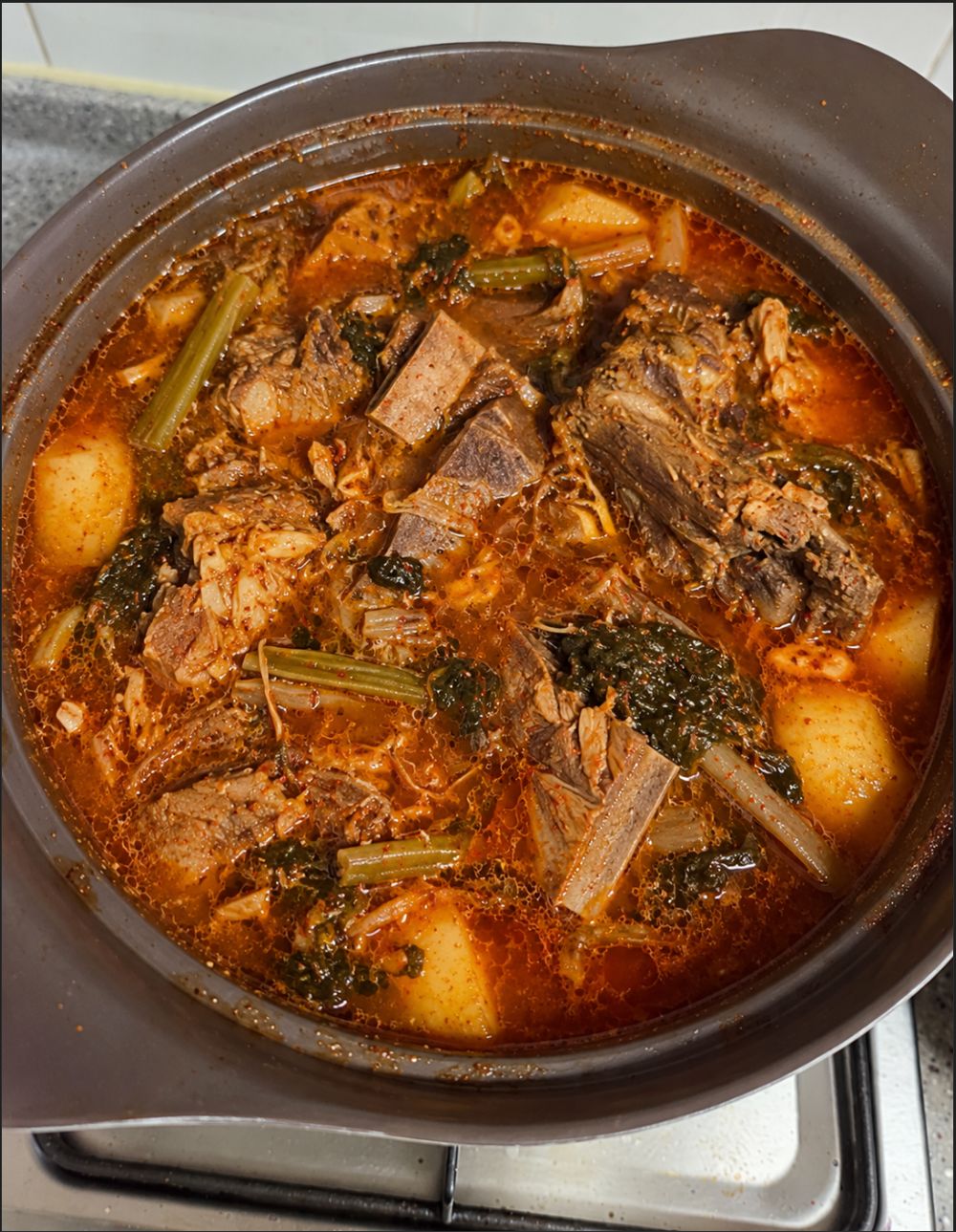 A large pot of gamjatang, Korean pork bone soup, filled with pork spine bones, potatoes, and perilla leaves in a deep red broth