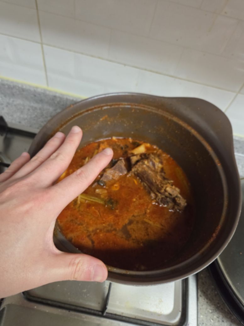 Leftover gamjatang in the pot after two meals, with one hand resting on the rim of the pot for scale